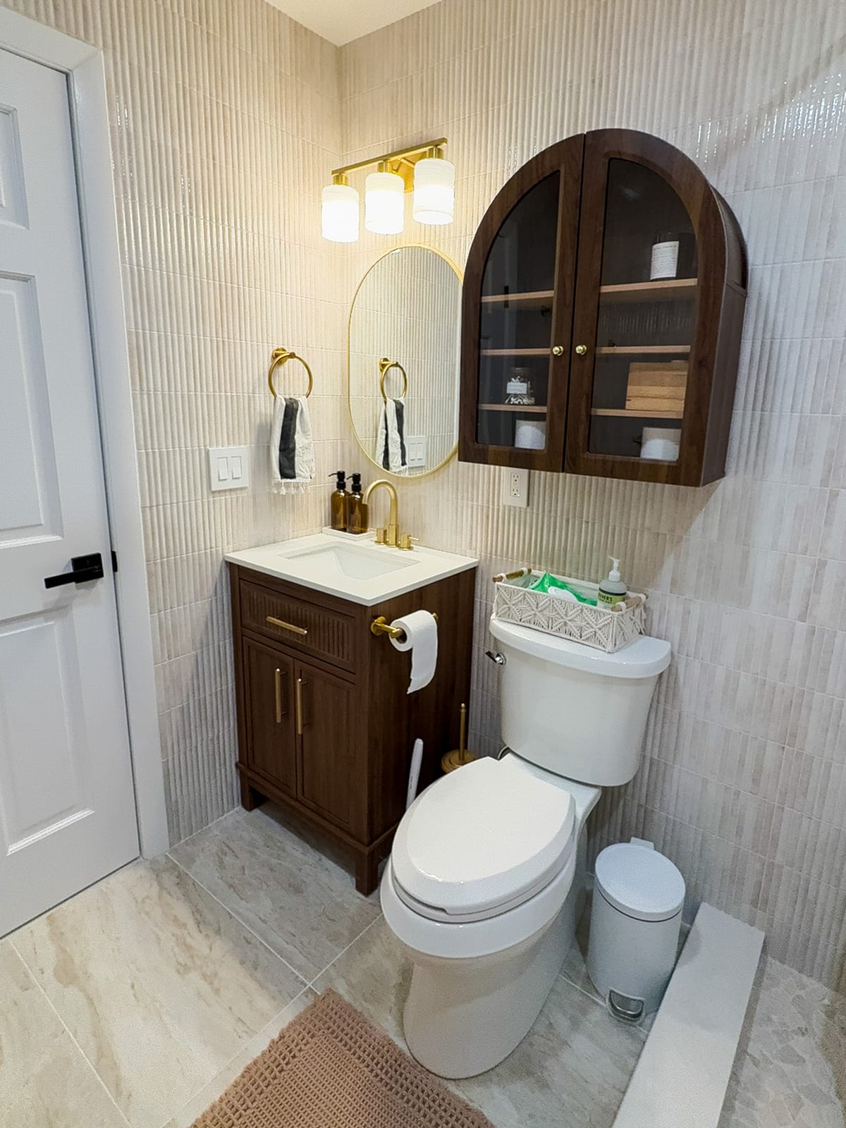 Wood vanity with white quartz top, gold faucet, and arched glass wall cabinet