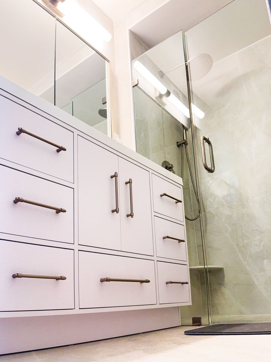 White multi-drawer vanity with brushed-nickel pulls beside a frameless glass shower